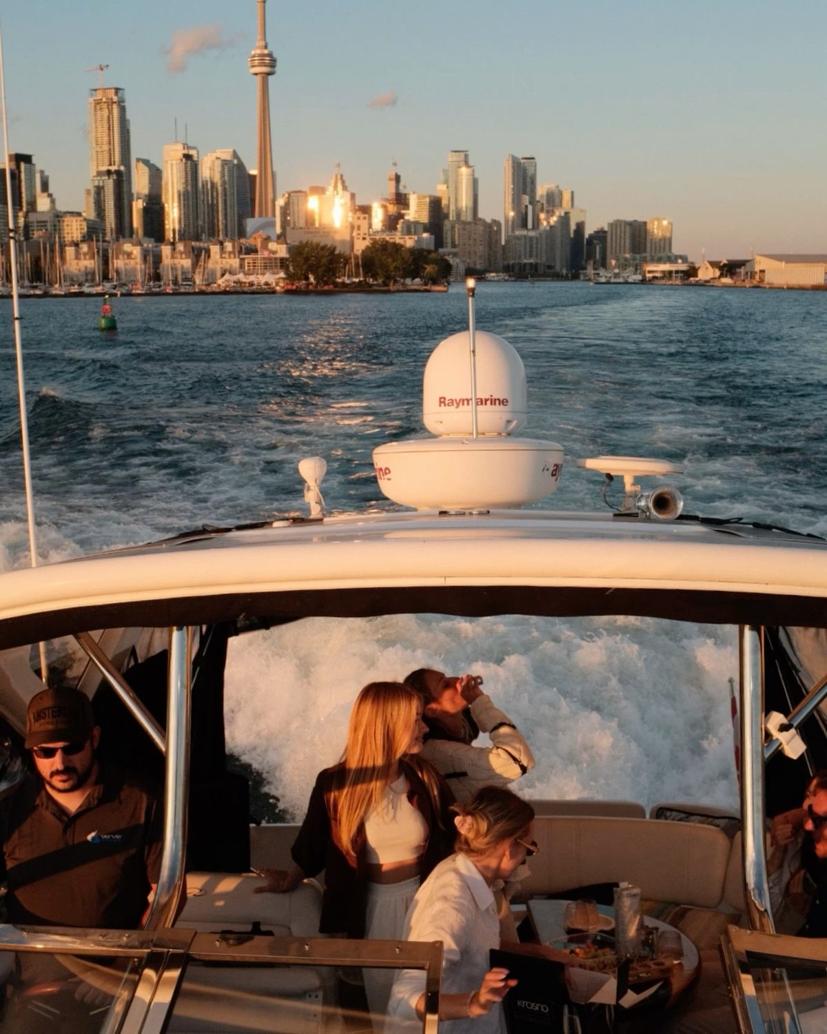 Friends relaxing on a small motorboat at sunset with the Toronto skyline behind them