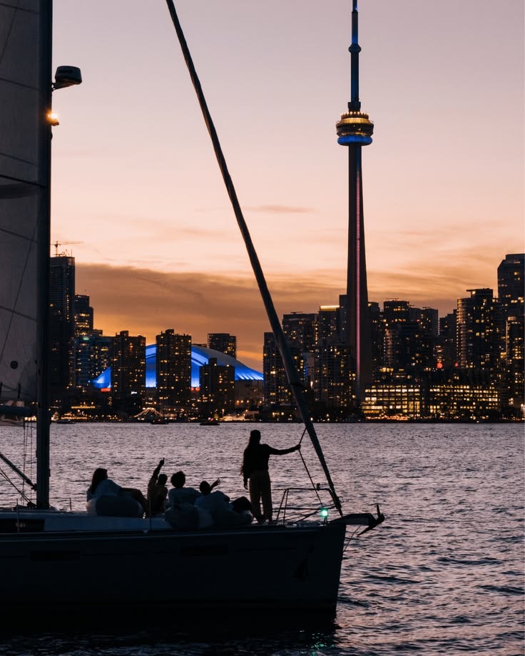 Silhouettes of friends on a boat at dusk facing the CN Tower